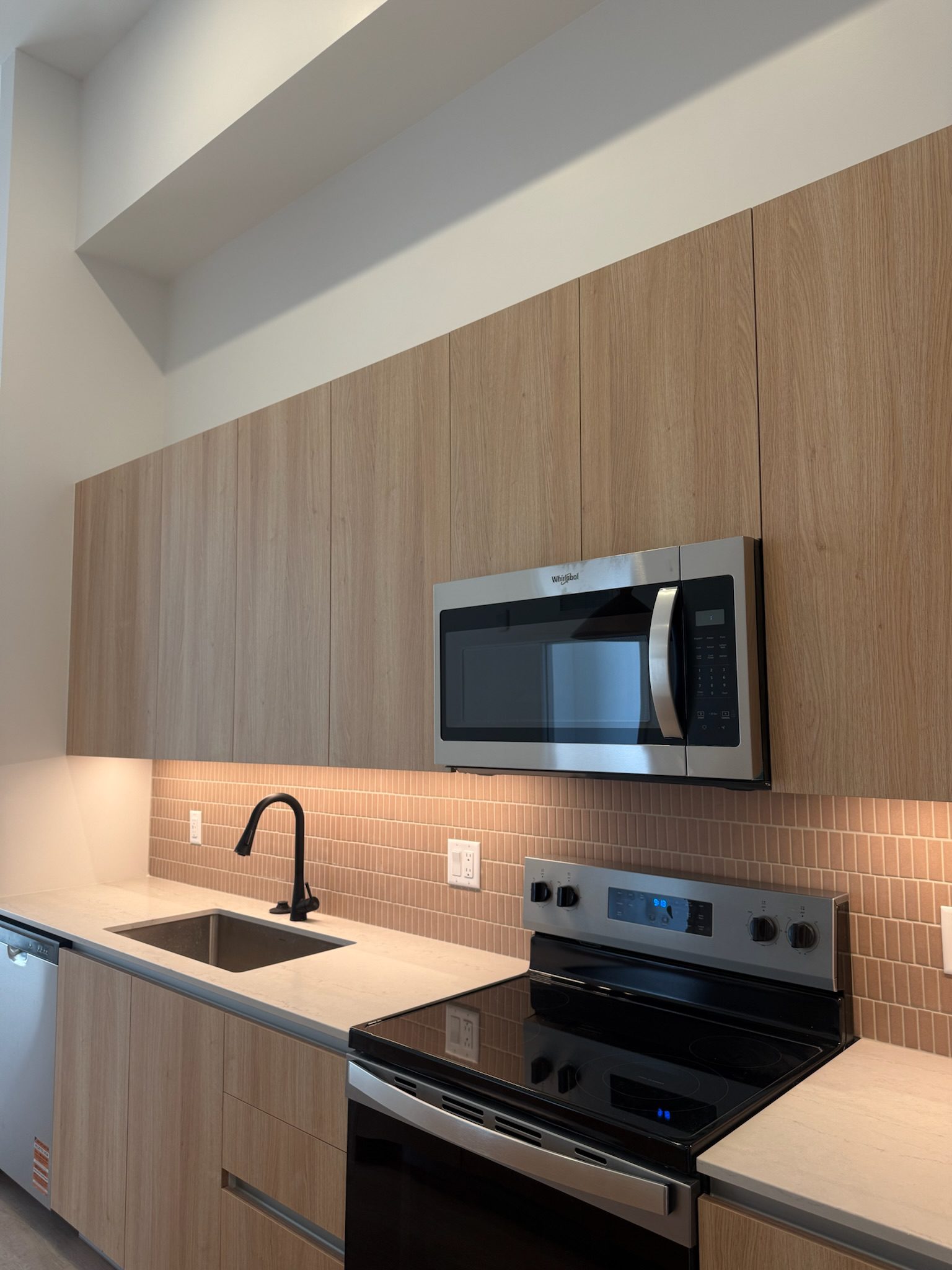 The 15th floor kitchen featuring marble countertops, a pink backsplash, brown pendants and accent lighting strips under the cabinets.