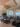A bright, modern Pilates studio with several black reformer machines, large mirrors on the walls, tall windows letting in natural light, and a view of the city outside. Decorative ceiling fixtures and plants add to the ambiance.